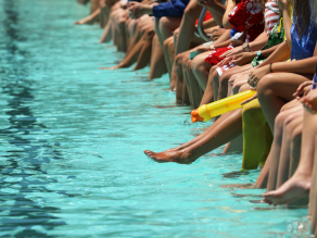 Viele Personen sitzen entlang eines Schwimmbeckens und kühlen die Füße im Wasser.