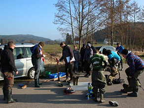 Eine Gruppe von Personen zieht sich auf einer Straße stehend Wathosen an.