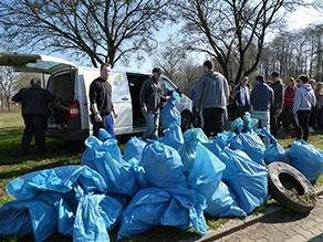 Mehrere Personen laden Müllsäcke in einen Transporter. Vor ihnen befindet sich ein großer Berg blauer Müllsäcke und ein LKW-Reifen.