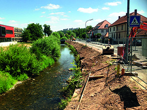 Die Brend im Bereich der Otto-Hahn-Straße: Die Böschung des rechten Flussufers wurde freigestellt. Ein Bauzaun trennt die Baustelle von einer Straße.