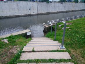 Eine Treppe mit Geländer führt zu einer Einstiegsmöglichkeit ins Wasser eines Flusses. Es besteht die Möglichkeit zum Kneippen und Abkühlen durch einen Handlauf, der entlang der Ufermauer angebracht wurde (Ilmdurchgang).