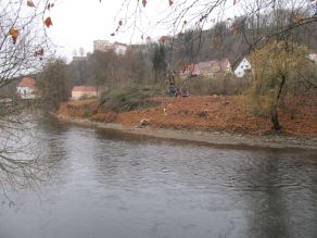 Die Uferböschung eines Flusses wurde von Gehölzen befreit. Baumaschinen und Buschwerk befinden sich oberhalb der Böschung.