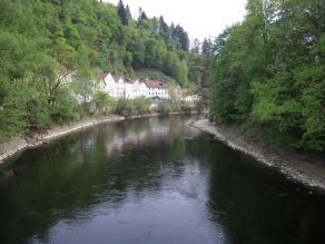 Fluss mit hartem Uferverbau durch Steinsatz und dichtem Ufergehölz.
