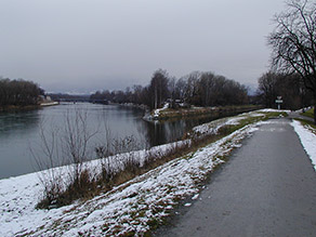 Blick von einem Hochwasserschutzdeich mit Geh- und Radweg auf das Innspitz mit dem Zusammenfluss von Mangfall und Inn. Die Ufer und Deichböschungen sind teilweise mit Schnee bedeckt.