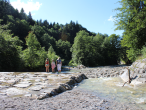 Mehrere Personen stehen im befestigten Flussbett des Lainbachs oberhalb einer Wildbachsperre und blicken talabwärts.