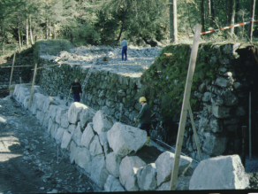Zum Bau der Wildbachsperre zur Ausleitung des Mühlbachs ist das Flussbett trockengelegt. Großformatige Wasserbausteine werden vor eine alte Sperre gesetzt.