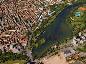 Luftaufnahme eines aufgestauten Flusses mit Algenbildung mitten in einer Stadt.