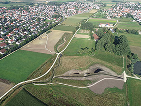 Luftaufnahme des letzten Bauabschnittes: Ein neuer Geh- und Radweg verläuft entlang eines renaturierten Baches. Wiesen- und Ackerflächen grenzen daran an. Im Hintergrund Siedlungsbereiche.