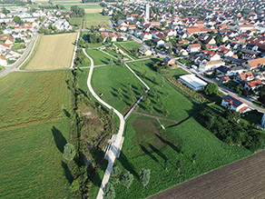 Luftaufnahme des Retzbachparks: Eine Grünanlage mit mehreren Geh- und Radwegen grenzt auf der einen Seite an einen renaturierten Bach und auf der anderen Seite an einen Siedlungsbereich.