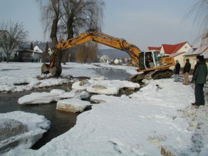 Ein Bagger arbeitet im Winter an einer rauen Rampe im Gewässerbett.