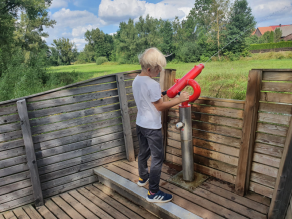 Ein blonder Junge spritzt an einer fest installierten Wasserspritzpistole aus Metall auf der Erlebnisplattform Wasser in die Vils.
