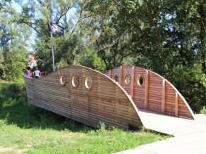 Kinder stehen auf einer Holzplattform am Ufer der Vils, das die Form eines Piratenschiffs hat. Sie bedienen eine fest installierte Spritzpistole.