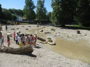 Eine Gruppe Kinder ist um einen Sitzstein an der Würm versammelt. Daneben fließt erstes Wasser durch das frisch hergestellte, kiesige Gewässerbett.