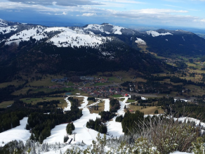 Vom Iseler Skigebiet reichen noch beschneite Abfahrten bis zum Ort Oberjoch. Ansonsten ist es unterhalb 1.600m weitgehend grün. Die eingeschneiten Fichten am Hang zeigen, dass es etwas Neuschnee gegeben hat.