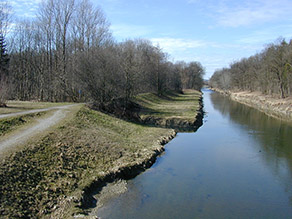 Mangfall in Rosenheim vor Beginn der Baumaßnahmen zur Deichrückverlegung. Das Gewässer ist schmal, die Ufer sind geradlinig, steil und mit Wasserbausteinen befestigt.